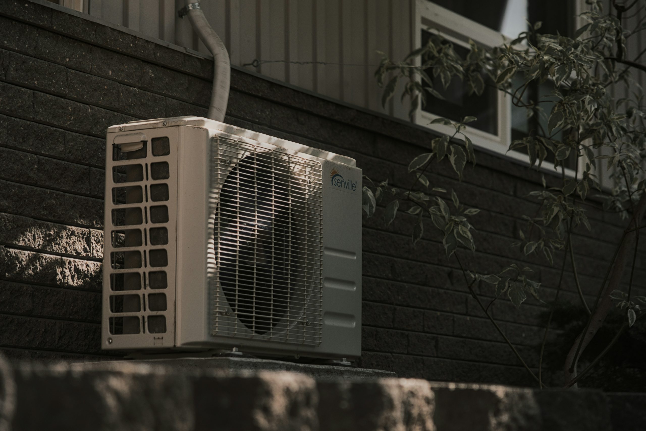 Outdoor HVAC unit installed on a residential home exterior, surrounded by shaded foliage. Ideal for illustrating energy-efficient air conditioning systems, HVAC installation, and home cooling solutions for sustainable comfort.