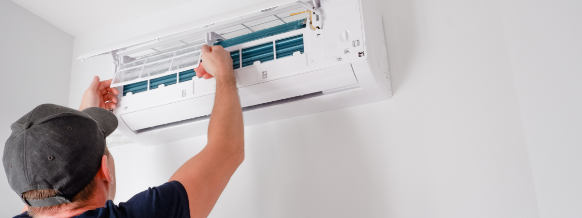 Technician cleaning or replacing the filter in a wall-mounted ductless mini-split air conditioner.