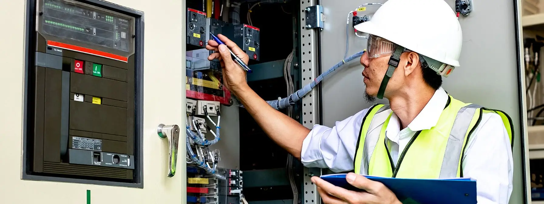 An electrician wearing safety gear inspects a residential electrical panel with a clipboard and pen in hand—demonstrating the importance of routine electrical inspections for home safety and efficiency.