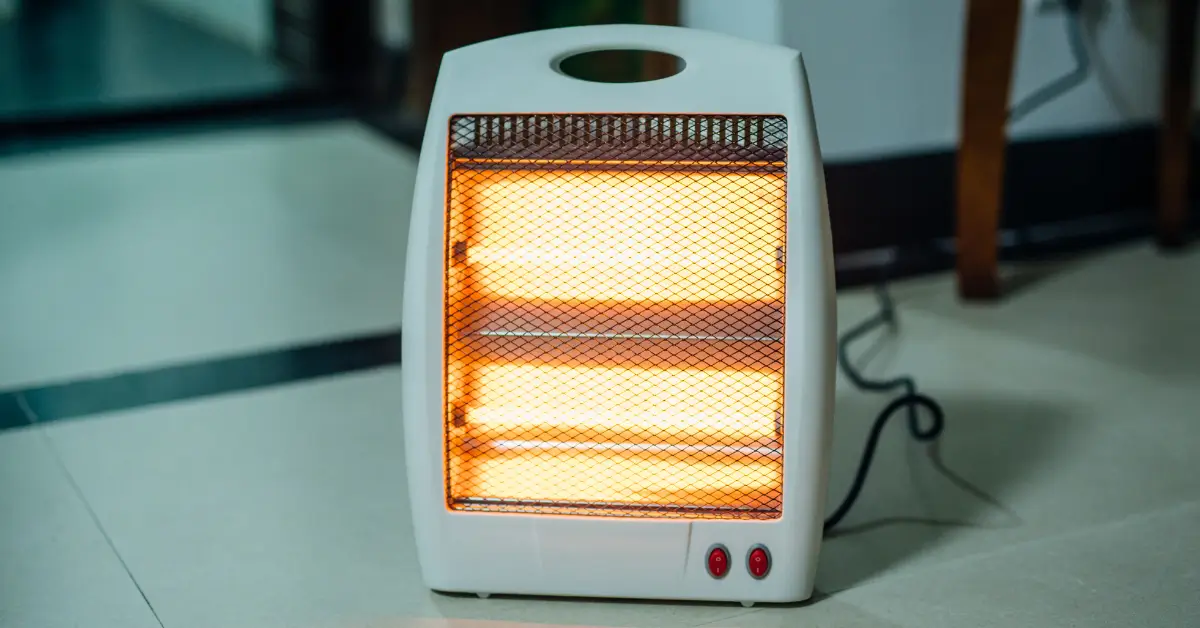 A white portable electric space heater with two glowing heating elements, placed on a tiled floor and turned on, emitting a warm orange light.